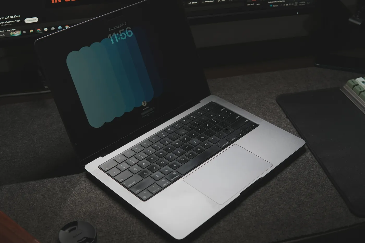A MacBook on a felt desk mat, its lock screen showing Saturday, July 5.